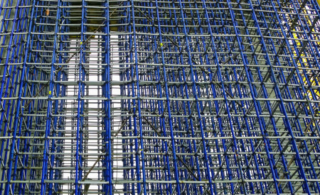 A complex arrangement of blue and silver scaffolding fills the construction site, reflecting sunlight and supporting ongoing work.の写真素材