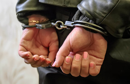 A person's hands are cuffed, showcasing the reality of arrest and the complexities of the justice system in a stark environment.の写真素材