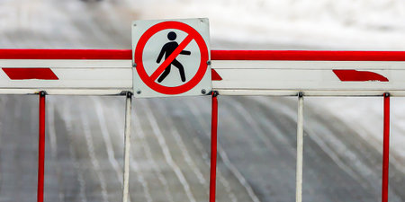 A bright warning sign indicates no entry for pedestrians alongside a snow-covered road, highlighting safety measures in winter.の写真素材