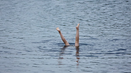 A pair of legs emerge from the water, creating ripples as they break the surface. The sunlight bathes the scene in a warm glow.の写真素材