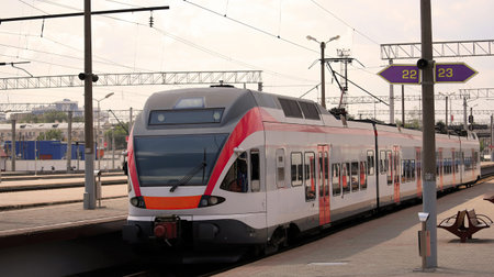 A sleek, modern train is stationed at an urban railway station, with platform signs displaying...
