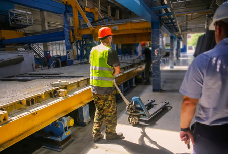 Workers in safety gear operate machinery for pouring concrete in a busy industrial factory setting...
