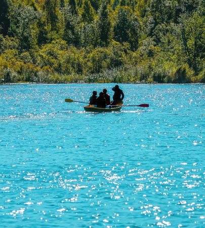 Four people enjoy a sunny day rowing on a vibrant turquoise lake surrounded by lush greenery