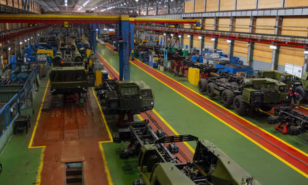Workers assemble military vehicles in a spacious factory, emphasizing industrial equipment and...