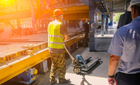 Worker in reflective vest and hard hat uses machinery for tasks in an industrial setting during a...