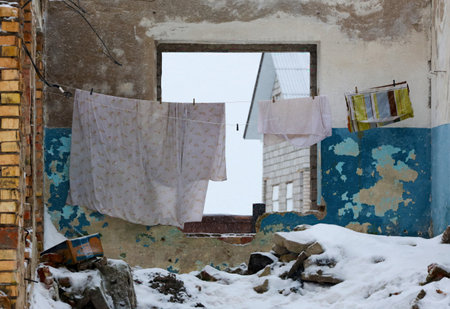 Clothes are drying on a line inside an abandoned building, surrounded by snow and debris, showcasing decay and neglect in winter.の写真素材