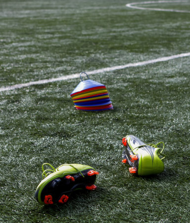 Bright soccer cleats are placed beside colorful training cones on a well-maintained artificial grass field during practice.の写真素材