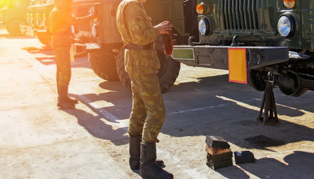 Soldiers perform maintenance on military vehicles during morning light at an army base