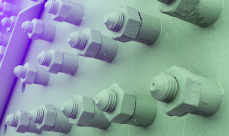 Metallic bolts and nuts are tightly secured on a large industrial structure, illuminated by warm sunlight, showcasing their intricate details.の写真素材