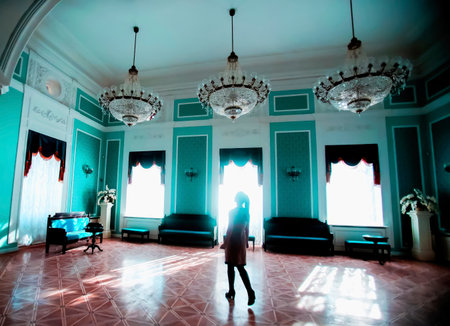 Bright turquoise walls and ornate chandeliers highlight a historic interior where a solitary figure observes the serene environment.の写真素材