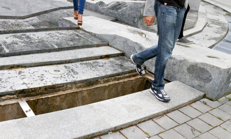 Two individuals navigate around a large opening in a decorative stone surface, showcasing urban design and safety concerns.の写真素材