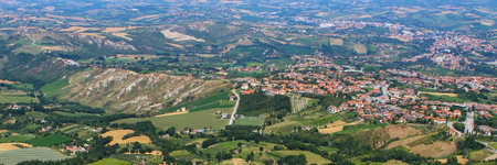 Aerial perspective captures a charming Italian village nestled among lush green hills, featuring terraced fields and distant mountains.の写真素材