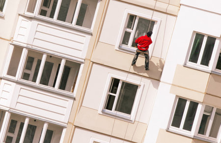 A worker is engaged in maintenance tasks, rappelling down the side of a tall residential building in bright daylight.の写真素材