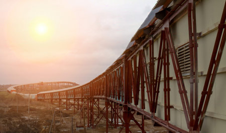 A railway track gracefully curves through an open landscape as the sun sets on the horizon, creating...