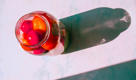 A glass jar filled with vibrant cherry tomatoes shows shades of red and orange, casting a prominent shadow on a light surface.の写真素材