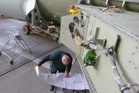 A technician examines a technical manual while inspecting critical components of an aircraft in a...