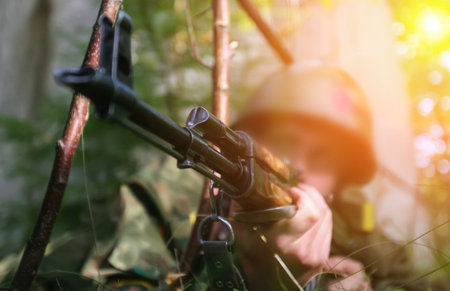 A soldier focuses on aiming a rifle while lying in thick foliage during a military training session as the sun sets.の写真素材