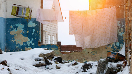 Clothes hang on a line in an empty, dilapidated structure as snow covers the ground, illuminated by the warm glow of sunset.の写真素材