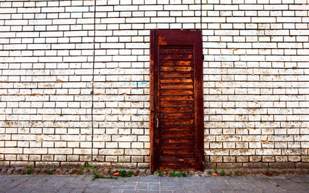 A rustic wooden door stands closed against a white brick wall in an urban area.の写真素材