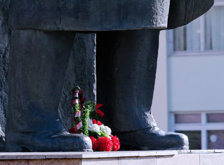 A wreath with flowers is arranged at the feet of a statue in a public space. It shows respect and...