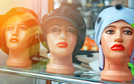 Three mannequin heads in a shop window display various hairstyles and hats under bright lighting,...