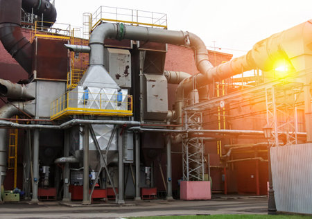 A large industrial facility shows pipes and machinery at work in a manufacturing area. The sun is...