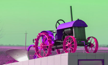 A bright-colored vintage tractor is fixed on a display near the roadside in an open field, with a...