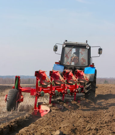 Tractor works the soil on a field to prepare for planting crops. The sky is clear above.