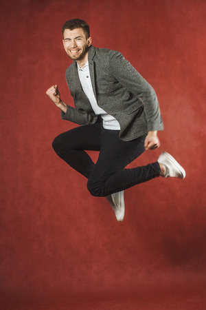 Photo of a young man on a red wall background looking at camera jumping.の写真素材