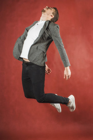 Photo of a young man on a red wall background looking at camera jumping.