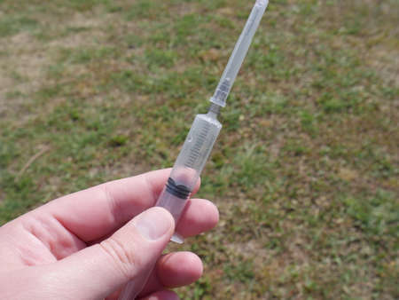 ampoule with red medicine in hand and a syringe on the background of faded grassの写真素材