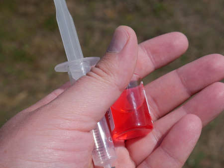 ampoule with red medicine in hand and a syringe on the background of faded grassの写真素材