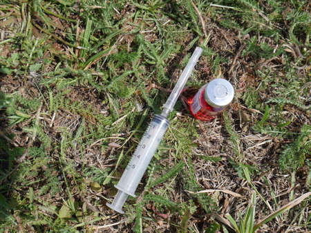 ampoule with red medicine and a syringe on the background of withered grassの写真素材