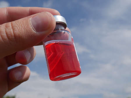 ampoule with red medicine in hand against the blue skyの写真素材