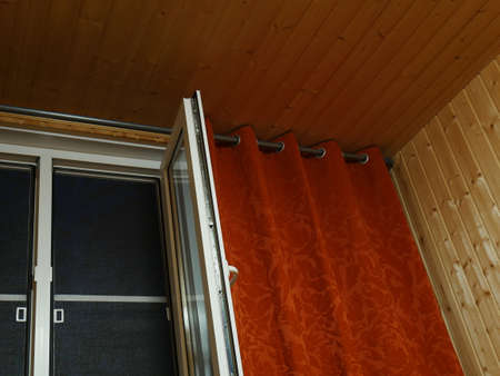 Plastic window and red curtains. It's dark outside. Finishing with natural wooden boards. Village.の写真素材
