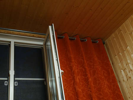 Plastic window and red curtains. It's dark outside. Finishing with natural wooden boards. Village.の写真素材