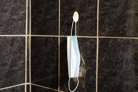 Daily medical mask for dressing on the street weighs on a hook. Against a dark wall.の写真素材