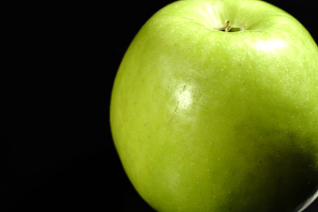 A green apple on a black background. Closeup. The light was dim.の写真素材