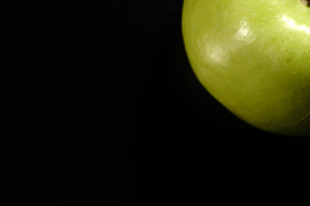 A green apple on a black background. Closeup. The light was dim.の写真素材