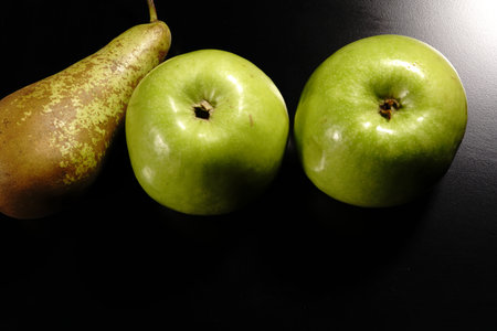 Two green apples and a pear on a black background. The view from the top.の写真素材