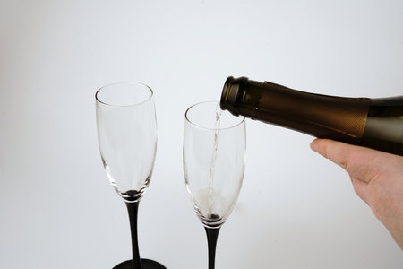 We pour champagne into glasses on a white background. A hand and champagne bubbles are visible.の写真素材
