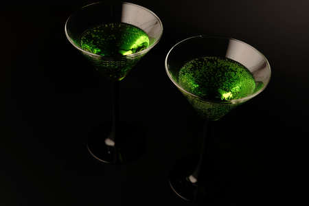 Two glasses with a green cocktail on a black background. One glass is full and the other is emptyの写真素材