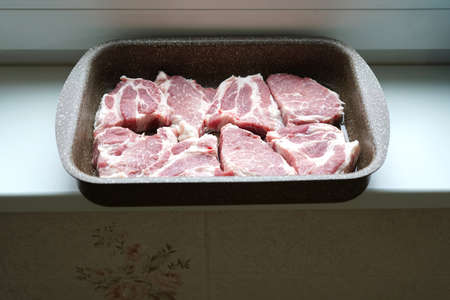 Raw pieces of pork laid in a bowl for further baking in the oven. In the kitchen.の写真素材