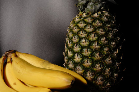 Pineapple and bananas on a black background. Dimmed lights.の写真素材
