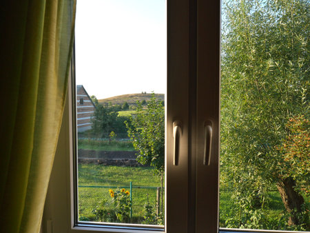Plastic window and outside the window you can see the house and a lot of grass with trees. Summer...