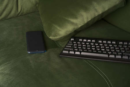 The keyboard and mobile phone are lying on the soft sofa.の写真素材