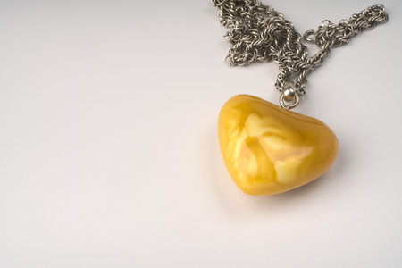 Moscow, Russia - june 18 2021: Decoration in the form of a large heart of golden color. Made of stone on a silver chain on a white background. Closeup. Space for the textのeditorial素材