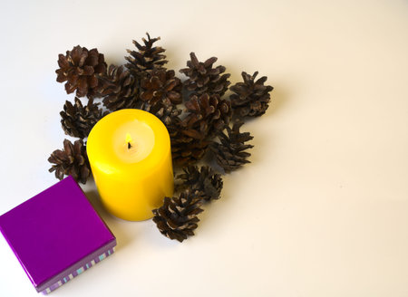 A large yellow candle and pine cones on a white background.の写真素材