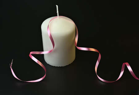 A large white candle with a pink gift ribbon on a black background.の写真素材