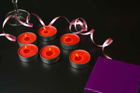 Burning small red candles and a champagne glass with a pink ribbon on a black background.の写真素材